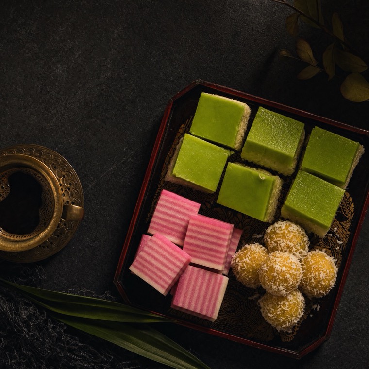 A tray of Malaysian kuih beside a brass cup of coffee